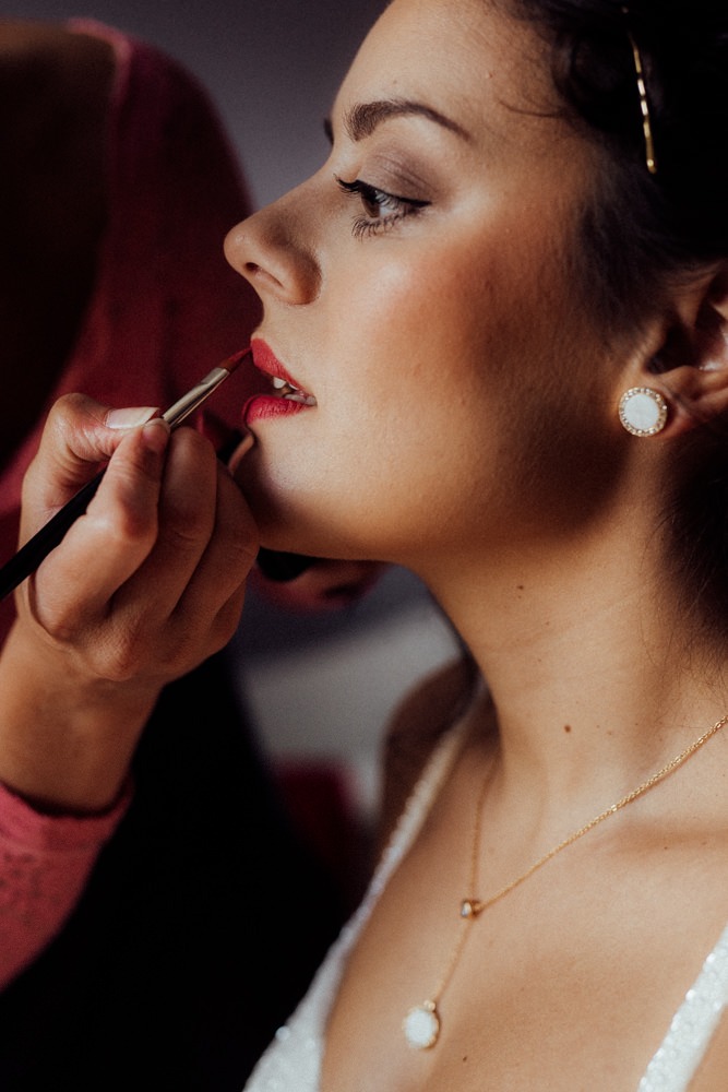 CloseUp Portrait einer Braut beim Getting Ready. MakeUp Artist trägt roten Lippenstift in Perfektion auf.