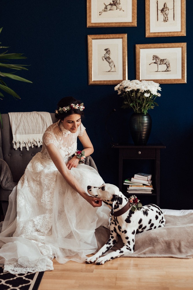 Braut mit Blumenkranz sitzt auf einem gemütlichen Ohrensessel, an ihren Füßen liegt ihr Dalmatiner.