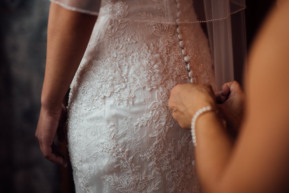 Brautmutter hilft der Braut beim Getting Ready ihr Kleid anzuziehen. Sie knöpft behutsam das Brautkleid zu.