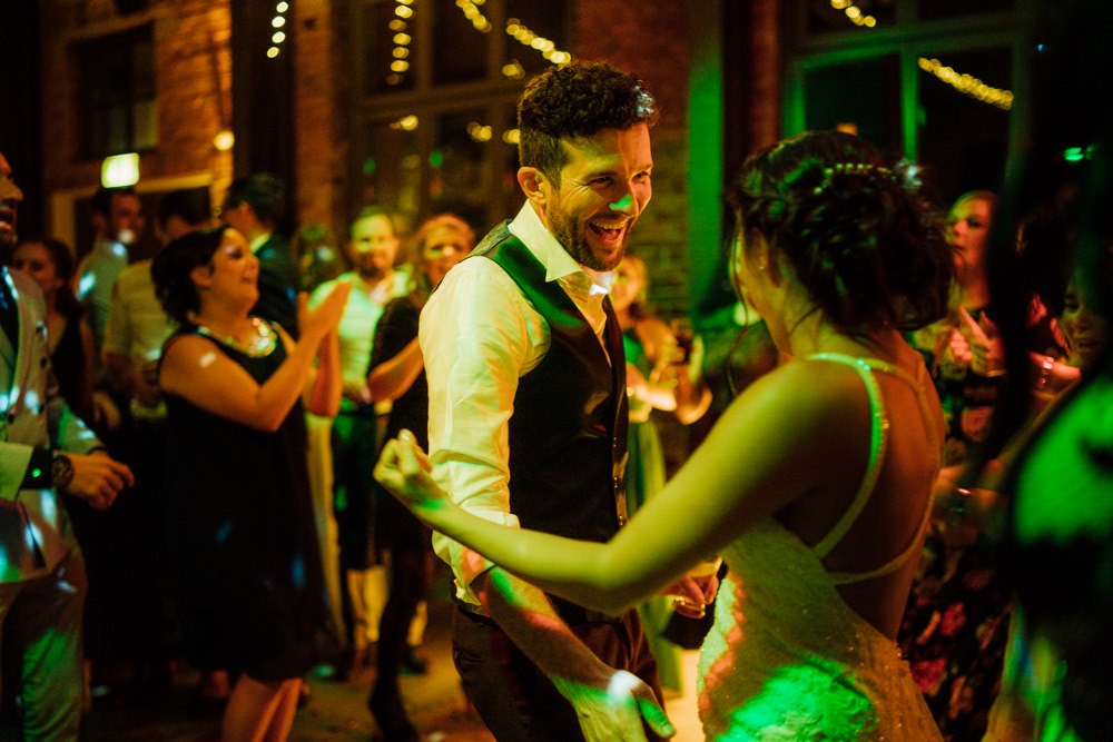 Brautpaar tanzt ausgelassen auf ihrer Hochzeitsfeier. Umgeben von ihren Freunden in buntem Partylicht.