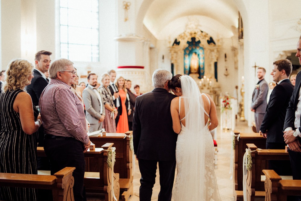 Braut schmiegt sich beim Einlauf in die Kirche noch ein letztes Mal an ihren Vater, der sie zum Altar führt.